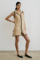 Vestido corto negro con cuello camisero, sin mangas, abotonado al frente y con aberturas laterales.