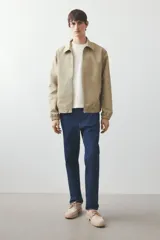 Campera color beige de denim rígido con cuello clásico, cierre frontal, bolsillos insertados al bies y un bolsillo interior. Elástico revestido en puños y bajo. Corte estándar y forrada.