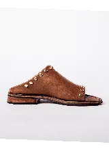 Sandalias de cuero color marrón claro, con punta descubierta y diseño tipo mule. Presentan tachas doradas en el borde superior y suela plana con pequeño tacón. Fabricadas en Uruguay.