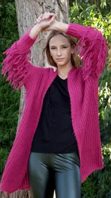 Saco tejido fucsia con flecos en las mangas, de corte holgado y largo a la altura de la cadera.