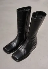 Bota de cuero negra, de caña media, punta cuadrada y taco bajo forrado.