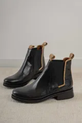 Botas Chelsea negras de cuero con elástico lateral y tirador trasero en color tostado. El talón tiene un detalle de cuero texturizado.