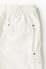 Short cargo color crema en popelina de algodón, con cintura elástica ajustable con cordón, bolsillos laterales y bolsillos con solapa y botones a presión en las piernas y atrás.