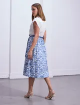 Vestido midi camisero de algodón con estampado floral en tonos azules y blancos. Tiene cuello solapado, cierre frontal con botones, manga corta, cintura elastizada con lazo de ajuste y bolsillos laterales.