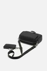 Bandolera negra de tela técnica con correa ajustable y extraíble. Tiene un compartimento principal con cierre de cremallera, un bolsillo interior con cremallera, un bolsillo frontal con solapa y hebilla de liberación rápida, y un monedero removible.
