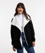 Cardigan alargado de punto pesado color negro, con cuello virada y forro de pelos sintéticos blancos. No tiene cierre y es de manga larga.