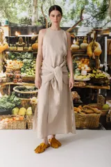 Vestido largo color beige, de lino, con cuello redondo y corte evasé. Tiene un lazo a la altura de la cintura y aberturas laterales.