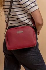 Bandolera pequeña de textura símil cuero color caramelo/marrón, con dos compartimentos principales con cierre. Correa ancha ajustable de tela negra con inscripción en relieve.