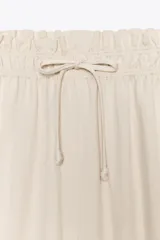 Pantalón palazzo color crudo, confeccionado en tejido fluido con mezcla de lyocell. Presenta tiro medio, cintura elástica ajustable con cordones, bolsillos laterales ocultos en costura y pierna ancha.