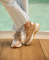 Zapatillas deportivas color beige con detalles dorados, cordones al tono y suela blanca.