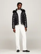 Campera puffer negra de nailon con relleno de plumón, capucha fija con ribete extraíble de pelo sintético, cuello alto, cierre de cremallera, bolsillos laterales con cremallera y parche con el logo de Tommy Hilfiger en la manga.