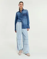Pantalón celeste de denim camisero liviano, corte pijama relajado, con cintura elastizada y tira de ajuste. Tiene bolsillos laterales, recortes en rodilla, cintura al corte con efecto deshilachado, jareta con tiras para regular en el ruedo y bolsillo plaqué en la espalda.