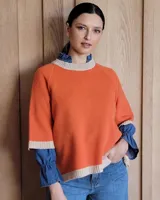 Sweater color naranja con cuello redondo y puños en color beige. Tiene mangas 3/4 y corte holgado. El cuello y los puños tienen terminación acanalada.