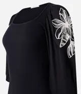 Blusa negra de rib con escote cuadrado, mangas largas abullonadas y bordado floral blanco en los laterales de las mangas.
