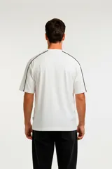 Remera de algodón color gris oscuro con efecto lavado, corte holgado y cuello redondo. Presenta un ribete blanco fino que recorre la costura del hombro y el borde de la manga.