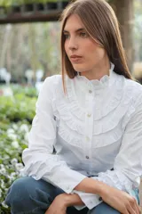 Camisa blanca de algodón con broderie, cuello alto con volados y mangas largas con puños abotonados y volados.