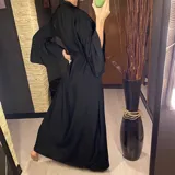 Vestido largo negro con botones frontales, abertura lateral y mangas anchas.