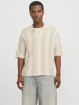 Polo de manga corta color crema con rayas verticales en relieve color verde claro. Tiene cuello clásico y cierre frontal con botones.