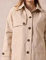 Gabardina impermeable color beige, marca Weatherproof, con abertura central con botones, bolsillos delanteros y capucha desmontable.