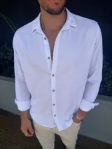 Camisa de lino color blanco para hombre, de manga larga con cuello tradicional y cierre frontal con botones marrones en contraste. Presenta un diseño de corte clásico y tejido ligero.