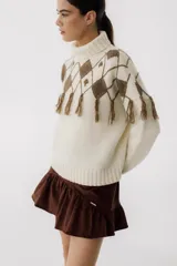 Sweater tejido de punto color crudo con cuello alto y diseño de rombos marrones con flecos.