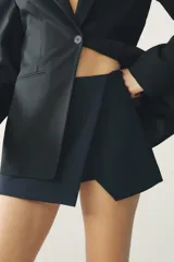 Falda pantalón corta color azul marino, de tiro medio, con abertura en el delantero y cierre lateral con cremallera oculta.