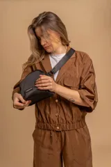 Bandolera pequeña de tela negra, con correa ancha ajustable y cierre superior.