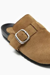 Zueco color beige con hebilla metálica ajustable, confeccionado en material símil gamuza y suela de goma negra.