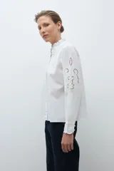 Camisa de algodón celeste claro, de manga larga, con cuello mao con volados y bordados calados florales en el frente y las mangas.