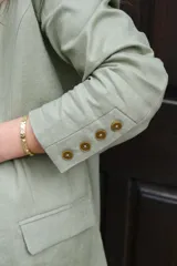 Blazer verde seco de lino, con corte entallado, solapas clásicas y cierre frontal con botones.