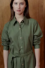 Vestido camisero corto color verde oliva con botones frontales, cinturón trenzado y volados en el ruedo.