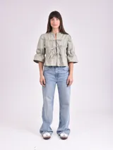 Blusa negra con escote mao y mangas 3/4 con volantes. Presenta detalle de frunces en el frente y lazos para ajustar.