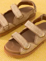 Sandalias bajas color beige con tiras de rafia y ajuste con velcro.