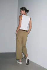 Pantalón cropped color beige de tiro alto y corte recto, confeccionado en algodón. Cuenta con bolsillos delanteros y traseros, trabillas en la cintura y cierre frontal con cremallera y botón.
