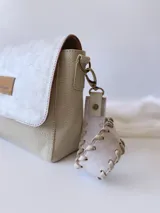 Bandolera color crudo con solapa de gamuza y cuerpo de cuero sintético texturizado. Tiene correa corta de cuero con tientos y forro de tela con bolsillo interno.