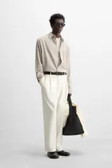 Camisa color crema de corte relaxed fit, confeccionada en tejido de mezcla de algodón suave al tacto. Tiene cuello solapa, manga larga con puños abotonados, un bolsillo de parche en el pecho y cierre frontal con botones.