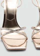 Sandalias doradas de tacón fino con tiras finas con strass y cierre de hebilla.