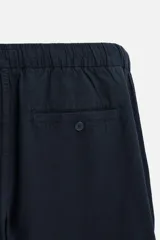 Pantalón azul marino de corte recto, confeccionado en tejido de algodón y lino. Tiene cintura elástica ajustable con cordón, bolsillos delanteros y traseros de vivo. Cierre frontal con cremallera y botón.