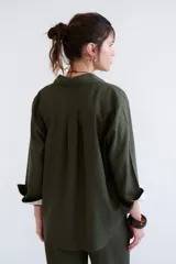 Camisa verde militar de manga larga con puños color crema, cuello clásico y cierre frontal con botones. Tiene un bolsillo en el pecho con bordado de una palmera color crema.
