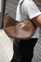 Cartera tipo lady bag color lila, de cuero sintético, con correa ajustable y herrajes metálicos plateados.