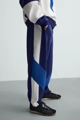 Pantalón deportivo azul marino con paneles laterales blancos y detalles en azul eléctrico. Corte relaxed fit, cintura elástica ajustable con cordón, bolsillos frontales ocultos y puños elásticos.