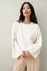 Sweater color beige de tejido de punto, con cuello redondo y mangas largas acampanadas con botones decorativos en los laterales.