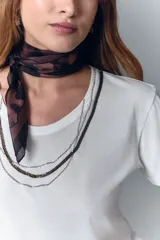 Remera blanca de algodón con cuello redondo y aplique de cadenas metálicas y strass en el escote.