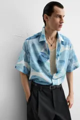 Camisa verde agua con estampado abstracto, corte relaxed fit, cuello solapa, manga corta y cierre frontal con botones.