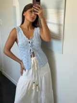 Top tejido de punto color celeste claro, sin mangas, con escote pronunciado en V y cierre frontal mediante lazos anudados. Presenta un patrón texturizado de cuadros.