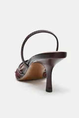 Zapato de tacón alto, destalonado, con punta fina. El cuerpo del zapato es de malla (mesh) color marrón oscuro, con apliques bordados y brillos en tonos similares. Posee una tira trasera elástica para ajuste.