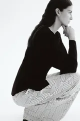 Pantalón de corte amplio y tiro alto, con cintura elástica y cordón de ajuste. Presenta un estampado geométrico en blanco y negro con líneas finas y formas entrelazadas.