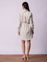 Vestido camisero corto a rayas verticales color beige, con cuello con solapa, abertura central con botones, bolsillos aplicados en el pecho y lazo de ajuste en la cintura.