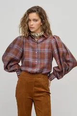 Camisa larga de lino a cuadros color avellana, con cuello camisero clásico, mangas largas abullonadas con puños elásticos, botones de nácar frontales y ruedo curvo, un poco más largo atrás. Incluye cinturón de cuero marrón.