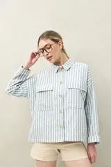 Chaqueta a rayas verticales celestes y blancas, con cuello camisero, cierre frontal con botones, dos bolsillos de parche en el pecho y mangas largas con puños abotonados.